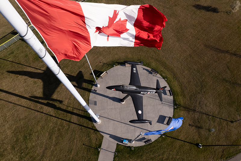 The Canadian & Albertan flags fly over a small plane mounted in a Leduc park.