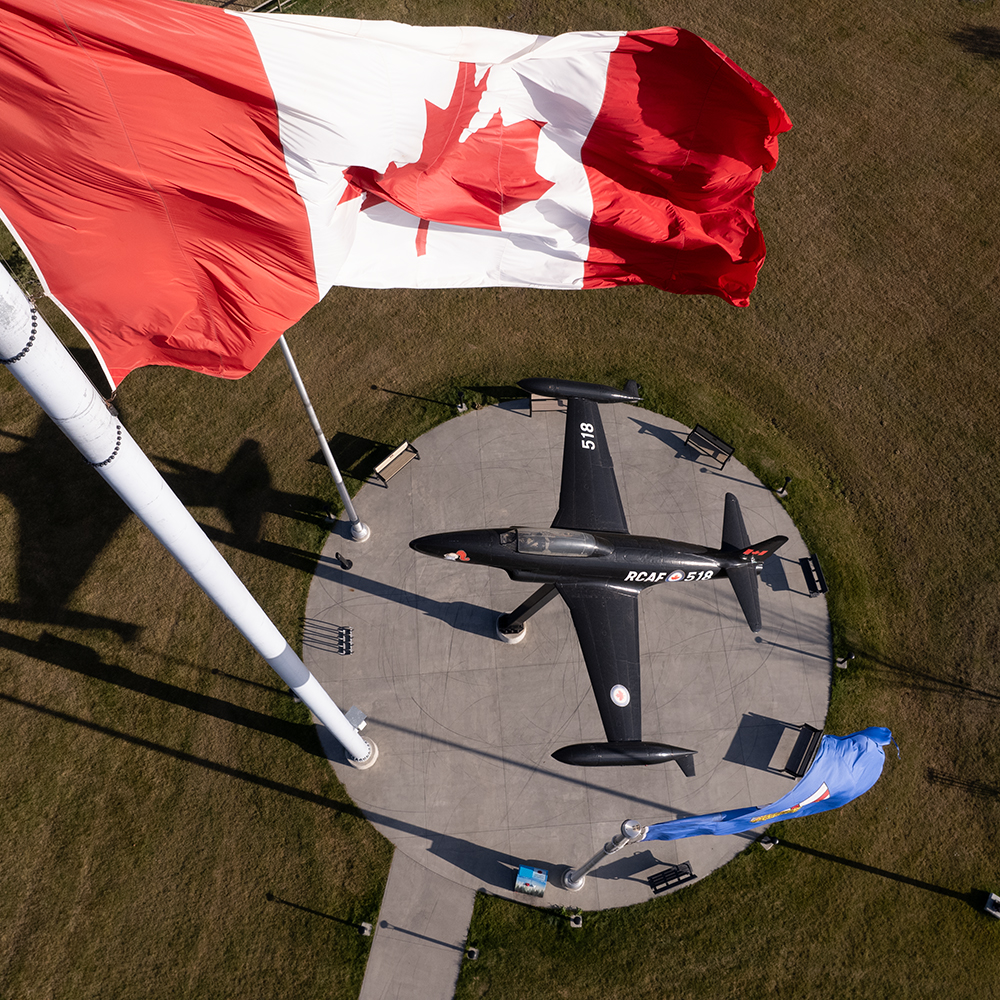 The Canadian & Albertan flags fly over a small plane mounted in a Leduc park.