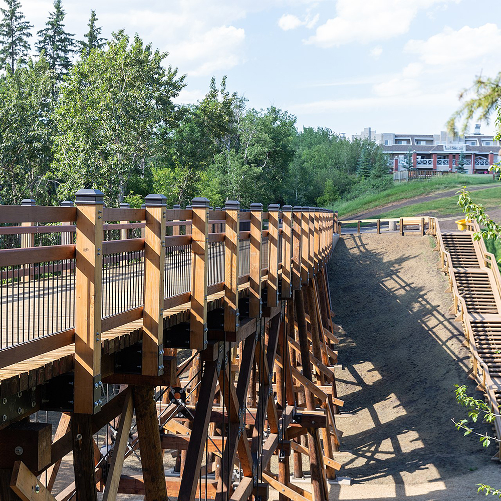 A Mill Creek Ravine pedestrian bridge, its terraces casting a shadow into the valley below, a forest beyond.