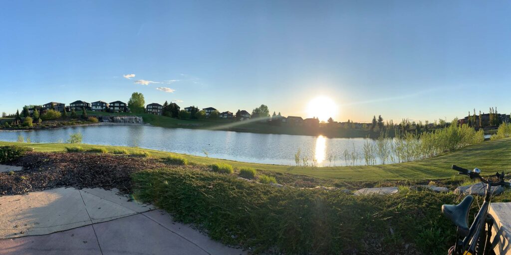 The sun low on the horizon over the Jagare Ridge Golf Club, a lake and homes in the background, a bike in the foreground.