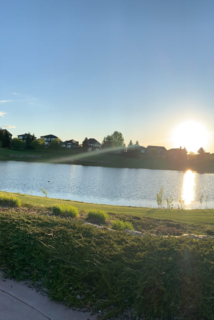 The sun low on the horizon over the Jagare Ridge Golf Club, a lake and homes in the background.