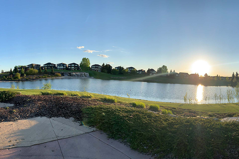 The sun low on the horizon over the Jagare Ridge Golf Club, a lake and homes in the background.