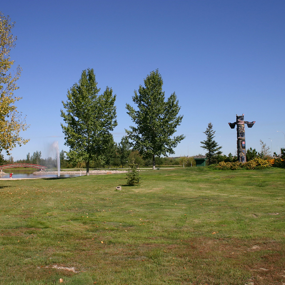 A fountain and statue near the Stony Plain Town Centre, surrounded by an expanse of green meadow and blue sky.