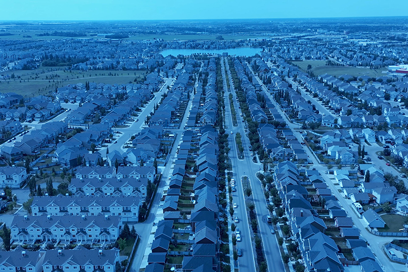 An aerial view of the Summerside neighbourhood. The image is tonally blue, with rows of homes and a lake in a centre focal point near the horizon.