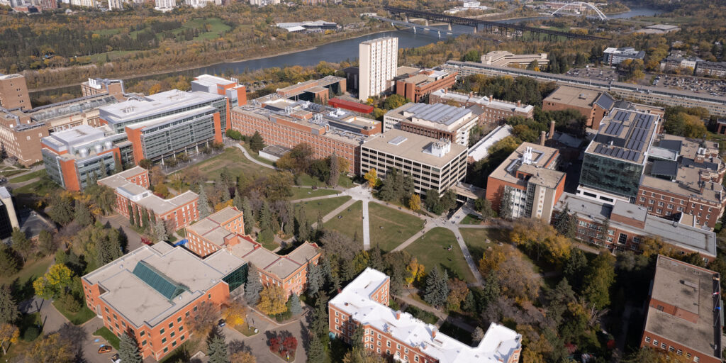 An aerial view of the University of Alberta in Edmonton. The campus is lush in early fall colours, with the river valley beyond.