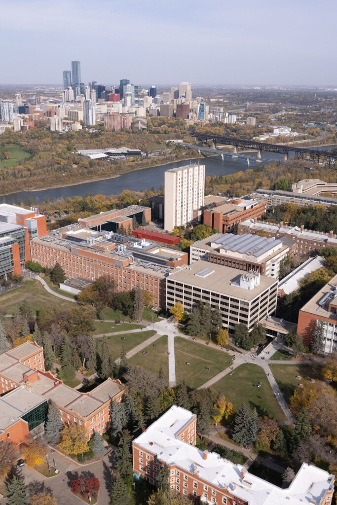 An aerial view of the University of Alberta in Edmonton. The campus is lush in early fall colours, with the river valley beyond.