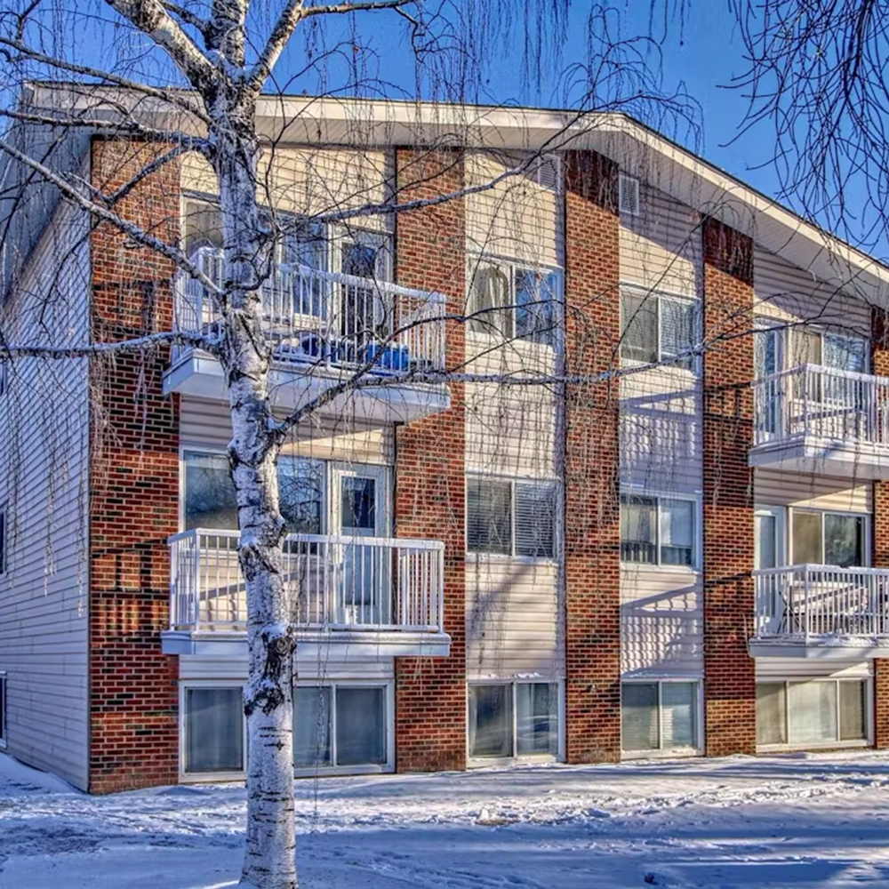 Exterior shot of an low-rise apartment building in Oliver. It's a snowy day with a blue sky.