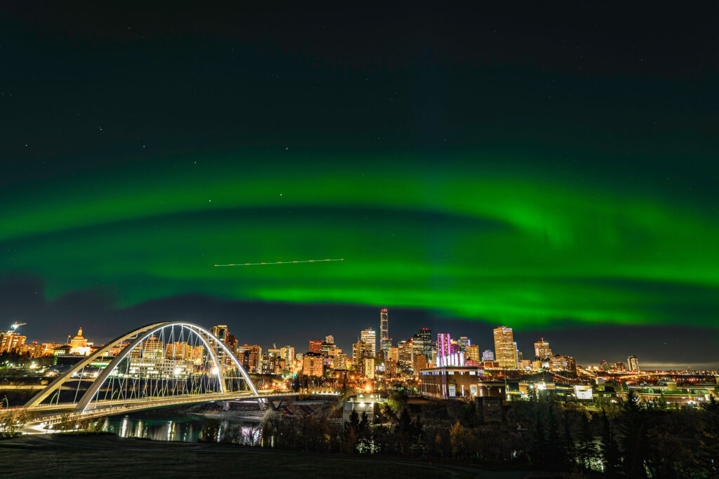 Green northern lights shine over Edmonton's river valley and skyline.