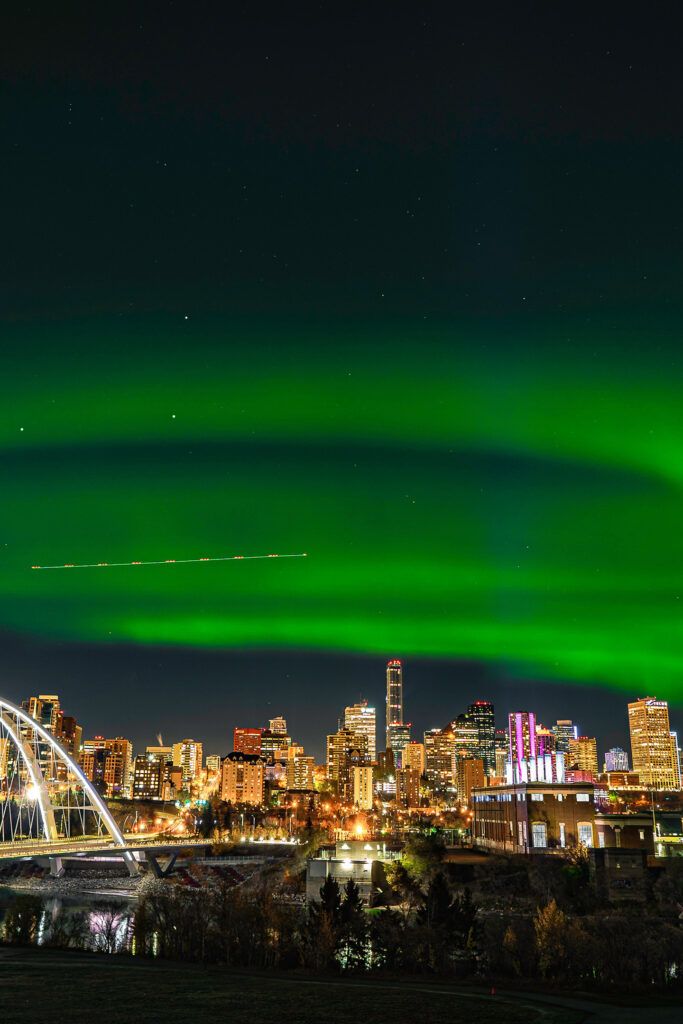 Green northern lights shine over Edmonton's river valley and skyline.