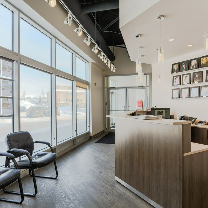 The reception area of our Fort Saskatchewan office. Two leather chairs sit in a room with dark hardwood floors, and a wood-panelled front desk. Photos of REALTOR®s line the walls behind the desk.