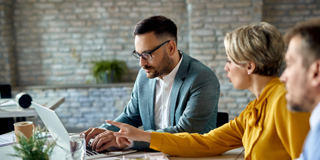 Real estate agent working on a computer while having a meeting with a couple in the office.