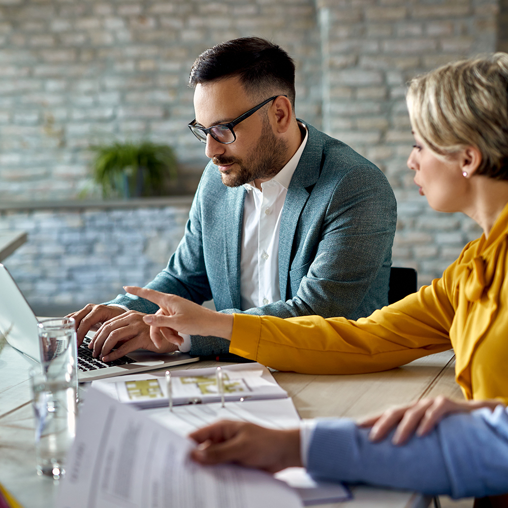 A real estate agent working on a computer while having a meeting with a couple in the office.