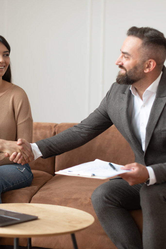 A real estate agent holding a clip board shakes hand with a young woman.