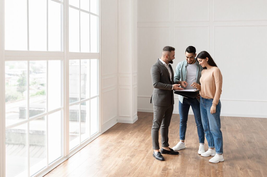 A smiling young couple discussing contract details, making agreement with real estate agent.
