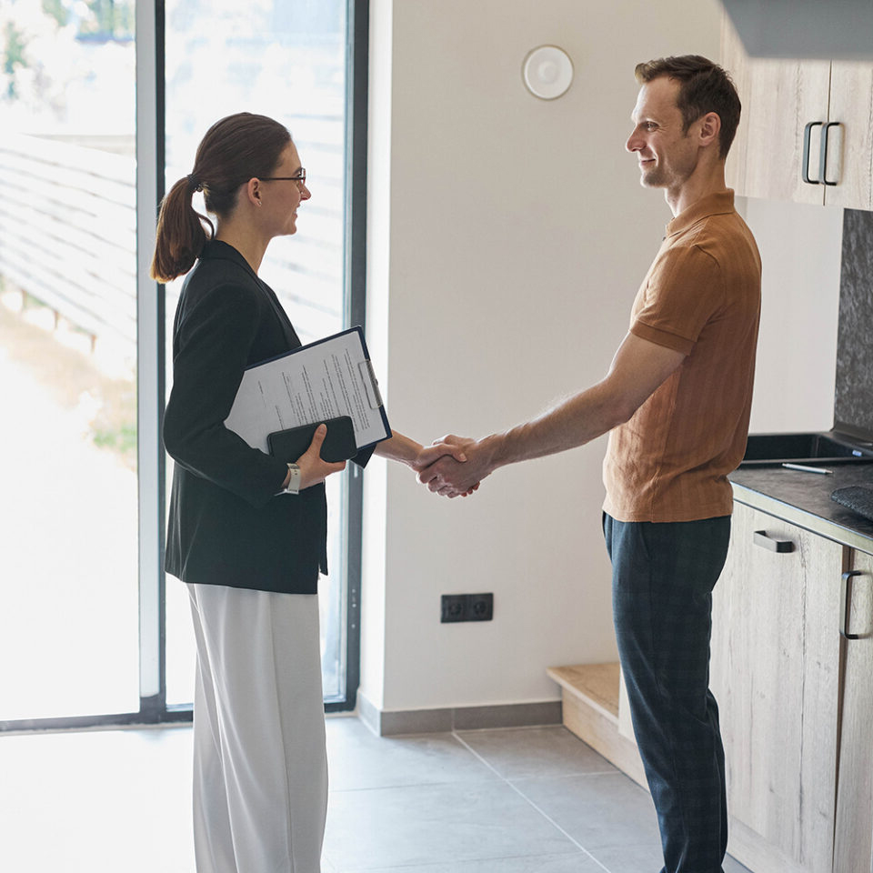 Two people stand in a kitchen shaking hands; a deal has been finalized.