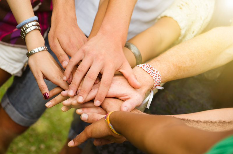 Multiple people stretching hands out, one on top of the other.