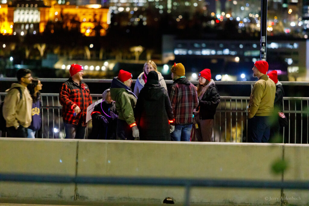 Walkers crossing the bridge with the Edmonton skyline glowing at night.