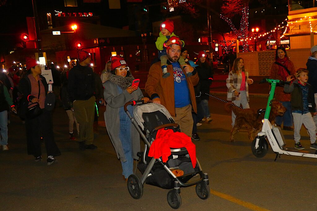 Families walking with strollers and scooters along the lantern-lit route.